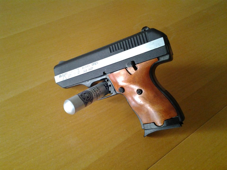 Pistol with wood-style grips and a rolled-up dollar bill inserted into the chamber