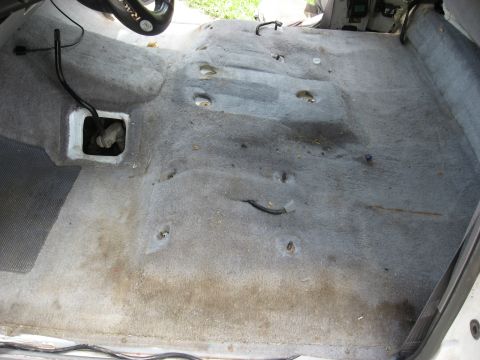 1994 Ford Bronco - The interior floor of a vehicle, stripped of its carpet, reveals numerous mounting points and exposed wiring.