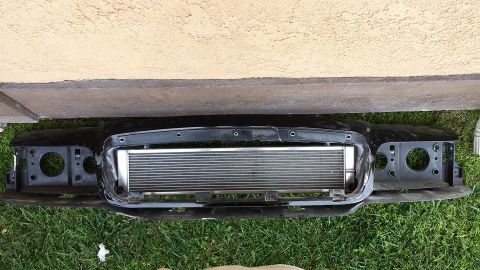 2003 Ford Crown Victoria - Black front bumper reinforcement holding a polished intercooler core, laid against a stucco wall on grass.
