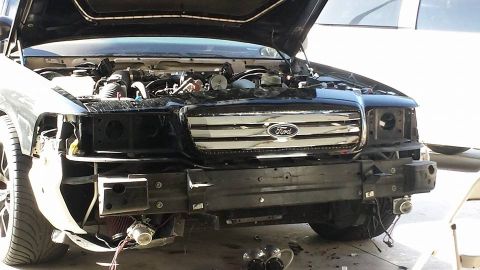 2003 Ford Crown Victoria - Front of a black Ford vehicle with the bumper cover off, showing the chrome grille with Ford emblem and a mounted intercooler.