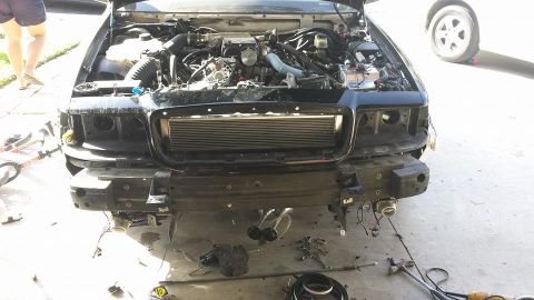 2003 Ford Crown Victoria - Sedan with hood up and front bumper cover off, exposing a front-mount intercooler and engine with parts on the driveway.