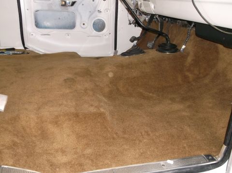 1979 Ford Bronco - The interior floor of a vehicle shows brown carpeting and a manual shifter, with the door panel removed.