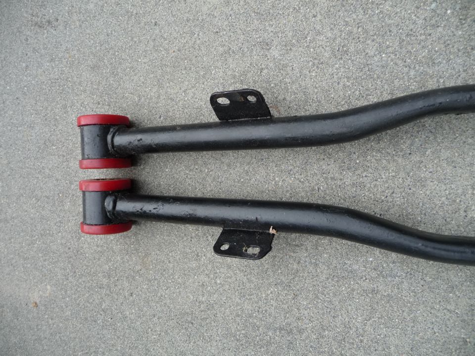 Pair of black control arms with red bushings on concrete