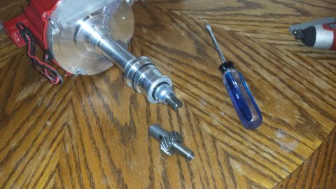1984 Ford Bronco - A red and silver automotive distributor, a detached gear, and a screwdriver are laid out on a wooden table.