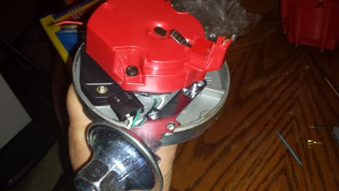 1984 Ford Bronco - A red plastic distributor cap with metal contacts and internal wiring is held by a hand.