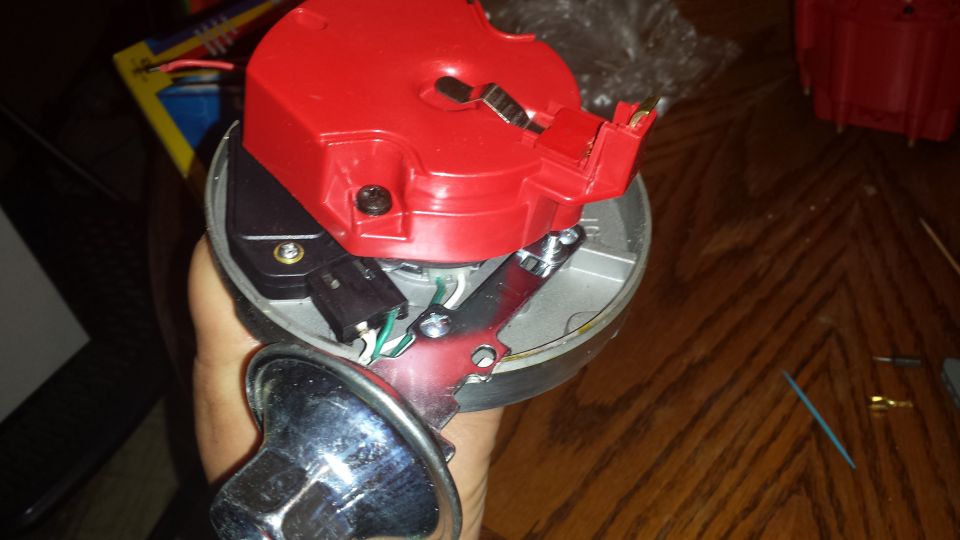 Red plastic distributor cap with metal contacts held by a hand, showing internal wiring