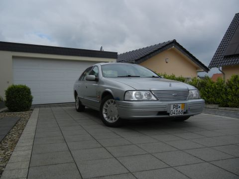 1999 Ford Fairlane - This silver sedan, identified by its grille badge, is parked in a paved driveway in front of a garage.