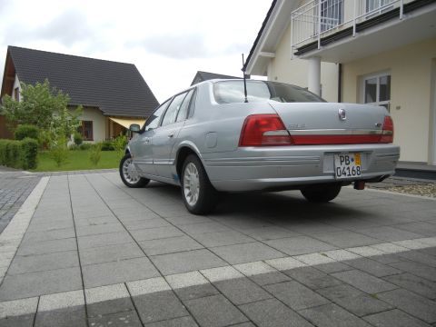 1999 Ford Fairlane - This silver sedan is parked on a paved driveway in front of a residential house.