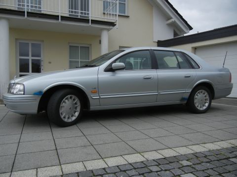 1999 Ford Fairlane - A silver sedan is parked on a tiled driveway in front of a modern house.