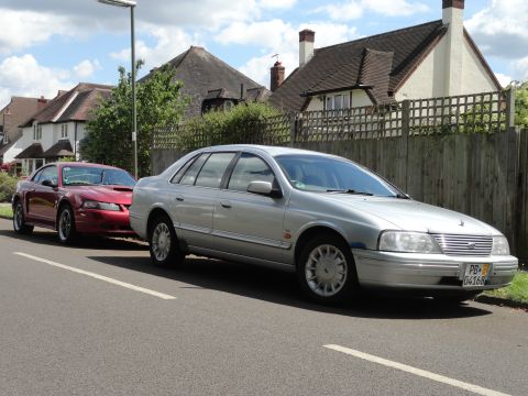 1999 Ford Fairlane - A silver sedan, possibly a Ford Fairlane, is parked on a residential street next to a red Ford Mustang.