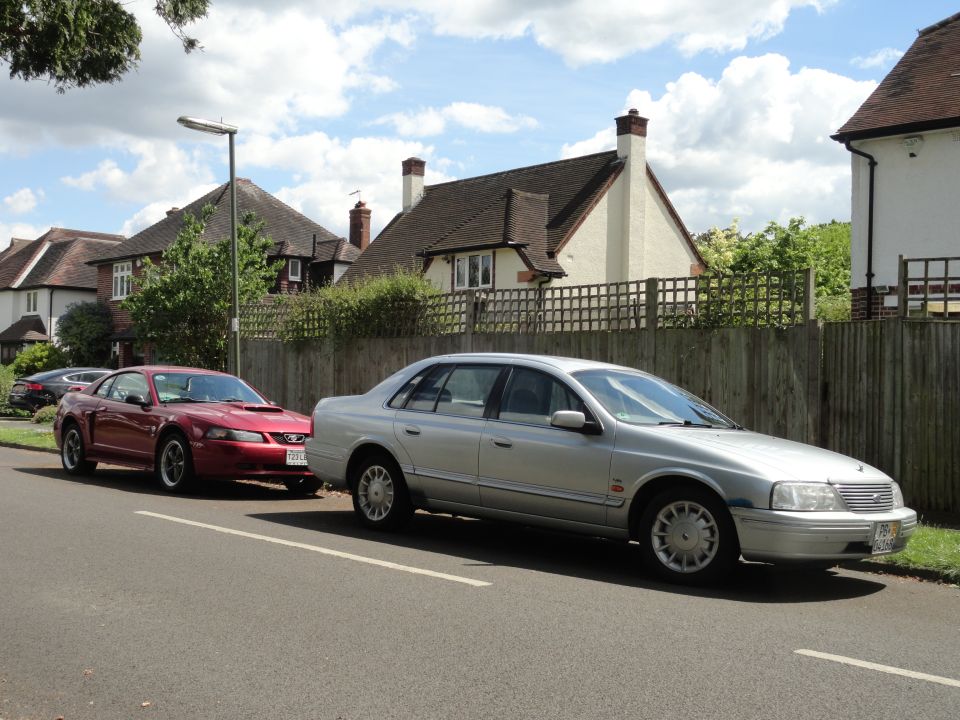Silver sedan parked next to a red Ford Mustang coupe on a residential street