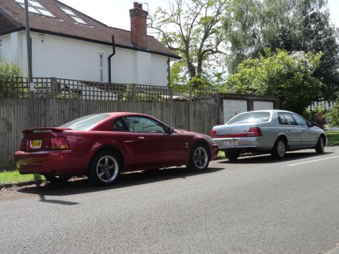 1999 Ford Fairlane - A silver sedan is parked on the street next to a red coupe.