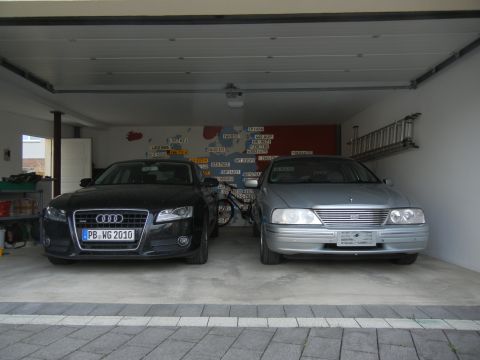 1999 Ford Fairlane - A silver sedan is parked in a garage next to a black Audi, with a map mural on the back wall.
