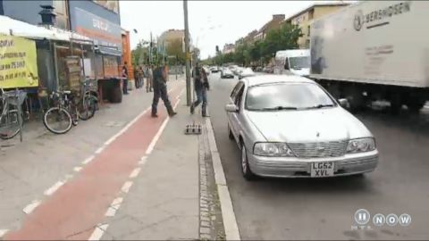 1999 Ford Fairlane - A silver sedan drives down a street with pedestrians and other vehicles present.