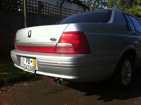 1999 Ford Fairlane - The rear of a silver Ford sedan is shown, its taillights, license plate, and dual exhaust system.
