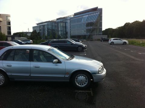 1999 Ford Fairlane - Silver 1999 Ford Fairlane sedan parked in a lot next to a modern office building.