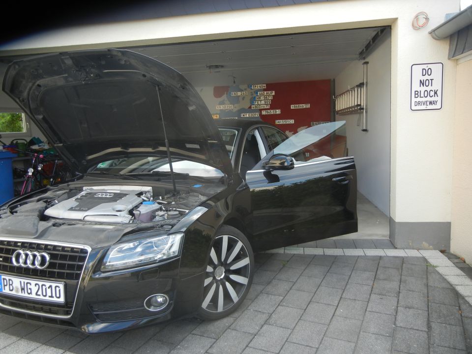 Black Audi with hood and driver door open, parked in a driveway. License plate reads PB WG 2010