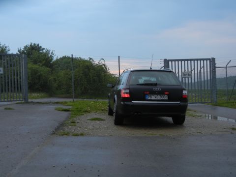 2003 Audi A6 - A black Audi A6 Avant is parked near a large metal gate under a cloudy sky.