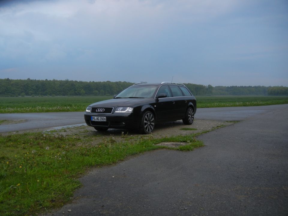 Black 2003 Audi A6 wagon parked on a wet road next to a grassy field