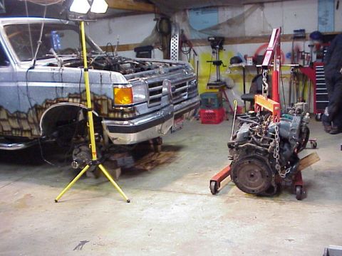 1989 Ford Bronco - A Ford truck is in a garage with its engine removed and placed on an engine stand.