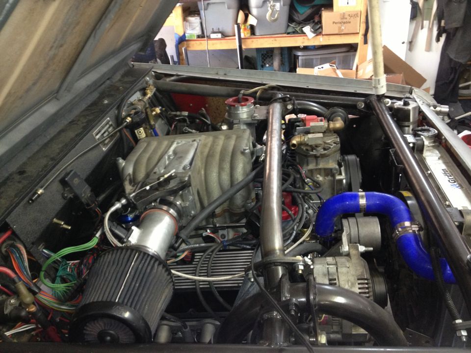 Engine bay with V8 engine, intake, and exhaust components. The hood is open