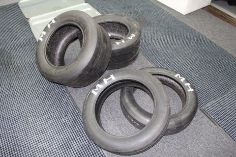 2003 Ford Crown Victoria - set of four M&H drag slicks resting on a textured gray floor with white M H markings.