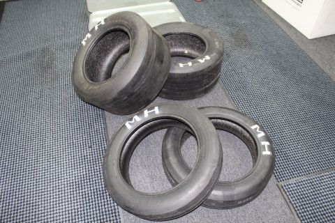 2003 Ford Crown Victoria - Four bias-ply drag slick tires marked M H grouped on a gray carpeted surface.
