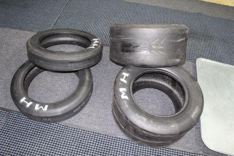 2003 Ford Crown Victoria - Four smooth drag slicks with M H lettering and a yellow paint mark on a gray floor.