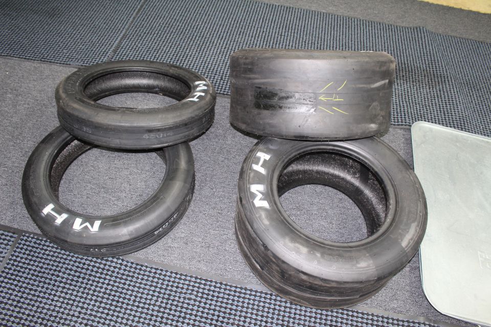 Four M H drag slicks with white lettering and yellow marks on gray carpet