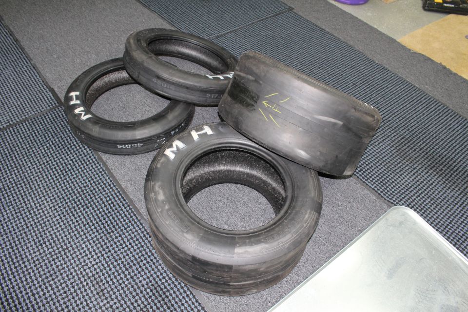 Assorted M H drag slick tires laid out on a gray carpeted surface