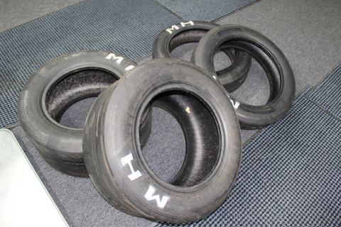 2003 Ford Crown Victoria - Four bias-ply drag slicks with white sidewall lettering grouped on a gray carpet.