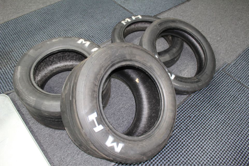 Four M A drag slick tires arranged in a cluster on gray carpet