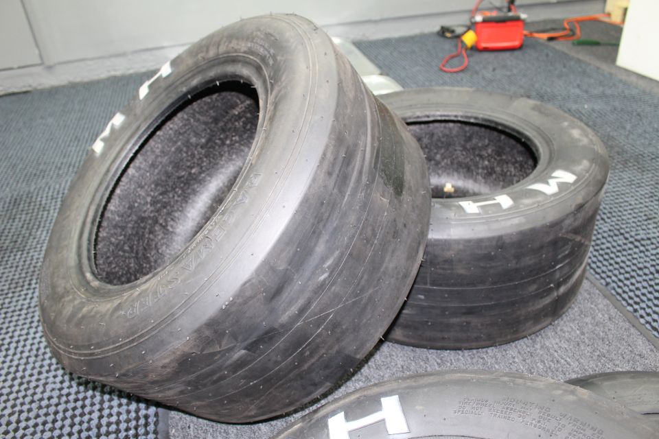 Pair of wide M H drag slicks resting on a blue-gray carpeted floor
