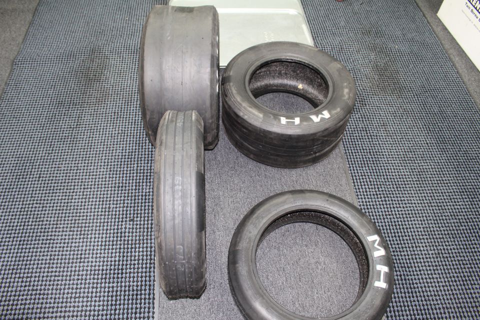 Four drag slick tires including ribbed front runners on gray carpet