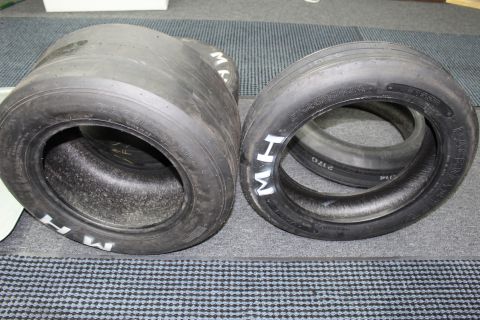 2003 Ford Crown Victoria - wide and a narrower M&H drag slick set side by side on a gray carpet.