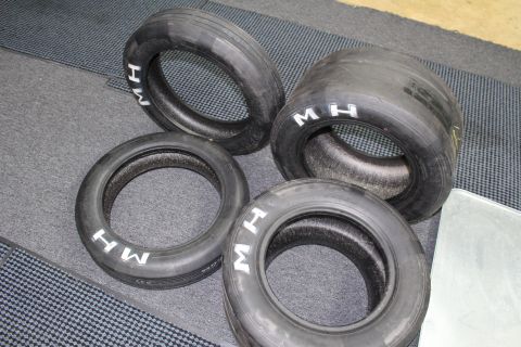 2003 Ford Crown Victoria - Four well-used drag racing tires marked with white "M H" sidewall lettering arranged on a gray rubber floor mat.