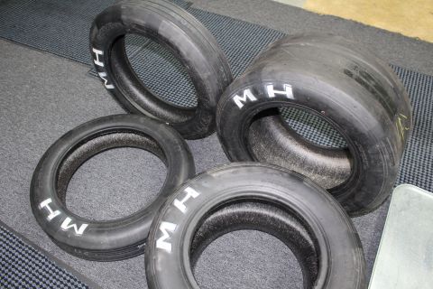 2003 Ford Crown Victoria - group of four worn drag racing slicks with white "M H" lettering grouped together on a gray textured floor.