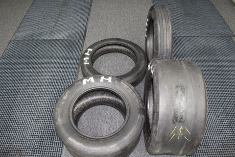 2003 Ford Crown Victoria - Several used drag racing tires, two with white "M H" lettering and one with yellow paint arrow marks, on a gray floor.