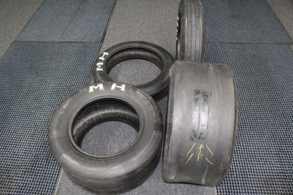 Worn slick tires, one with yellow arrow marks, on dark gray floor mat