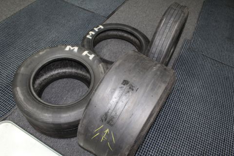 2003 Ford Crown Victoria - Used drag racing tires laid on a gray floor mat, one bearing yellow painted arrows and others marked with white "M H".