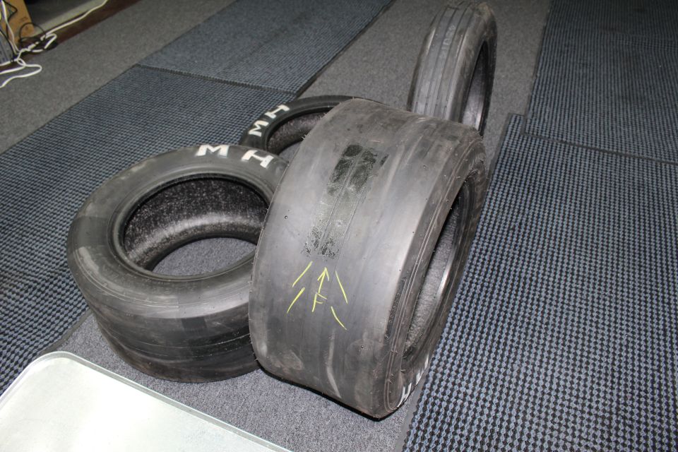 Wide slick tire with yellow arrows beside M H lettered tires on gray floor