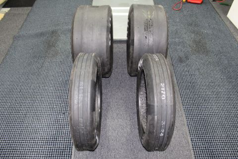 2003 Ford Crown Victoria - Four drag racing tires stood upright in two rows on a gray floor, sidewalls showing faint handwritten markings.