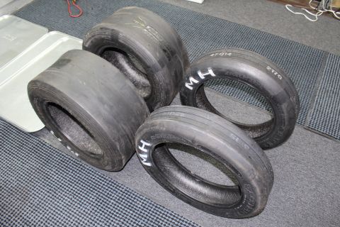 2003 Ford Crown Victoria - Four worn drag racing slicks on a gray floor, sidewalls marked with white "M H" and handwritten codes.