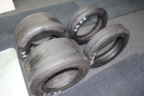 2003 Ford Crown Victoria - Bald drag racing slicks grouped on a gray floor, several bearing yellow arrow marks and white "M H" lettering.