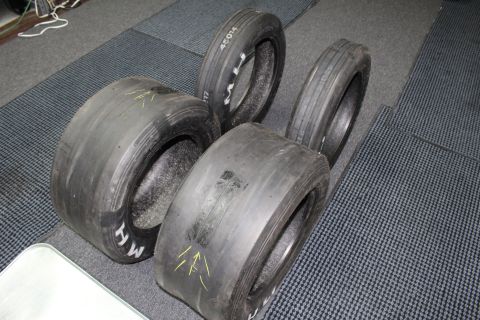 2003 Ford Crown Victoria - mix of wide slicks and narrow front-runner tires with yellow arrow marks and white "M H" lettering on a gray floor.