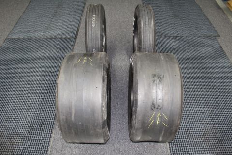 2003 Ford Crown Victoria - Four drag racing tires arranged in two stacks with yellow painted arrows visible on the treads, on a gray floor.
