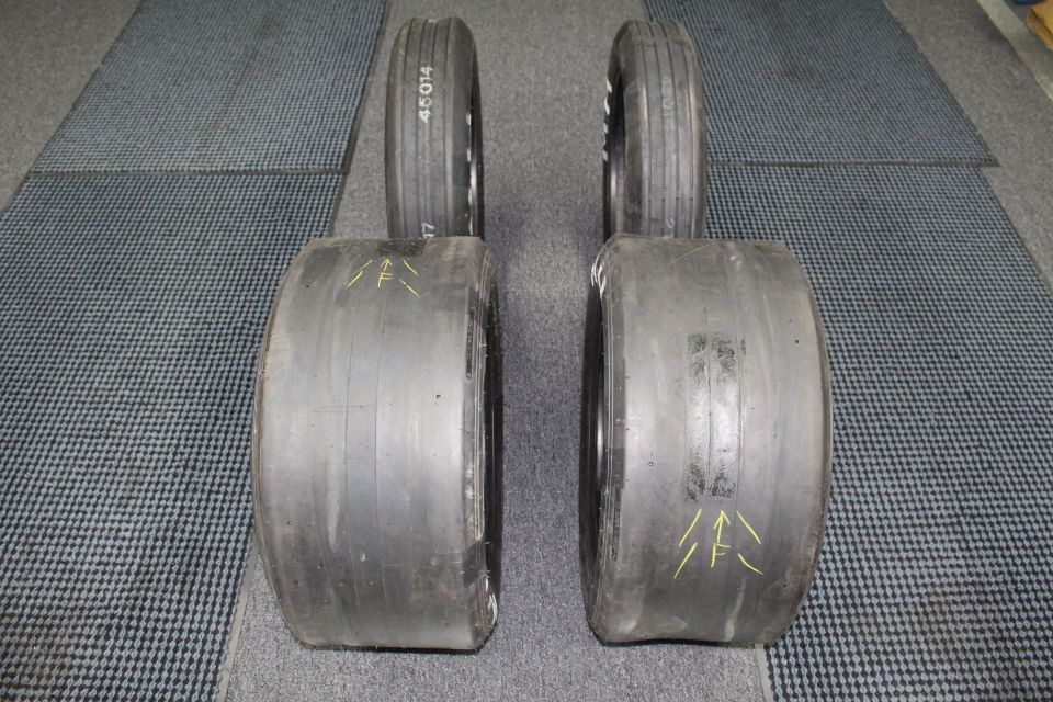 Four drag tires in pairs with yellow arrow marks on gray floor mat