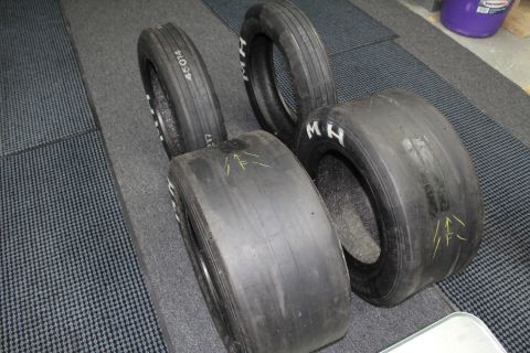 2003 Ford Crown Victoria - Drag racing tires of varying widths with white "M H" lettering and yellow arrow marks on a gray textured floor.