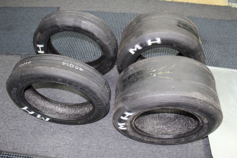 2003 Ford Crown Victoria - set of drag racing tires on a gray floor showing white "M H" lettering, handwritten codes and yellow arrow marks.