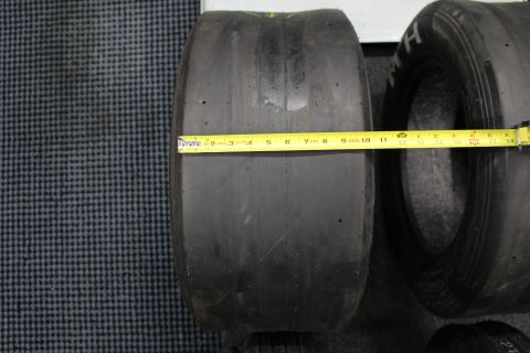 2003 Ford Crown Victoria - wide drag racing slick laid on its side being measured across the tread with a yellow tape measure.